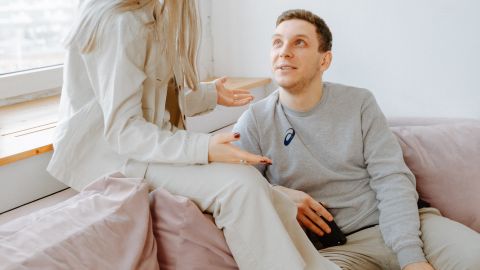 A couple having a conversation on a pink couch in a well-lit modern apartment.
