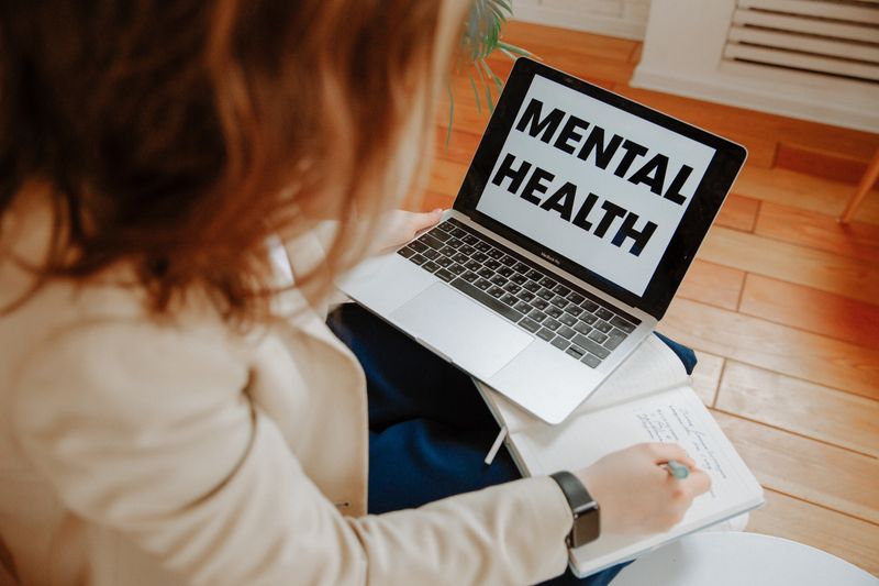 Uma mulher participando de uma sessão de terapia online, tomando notas com um laptop exibindo 'Saúde Mental'.