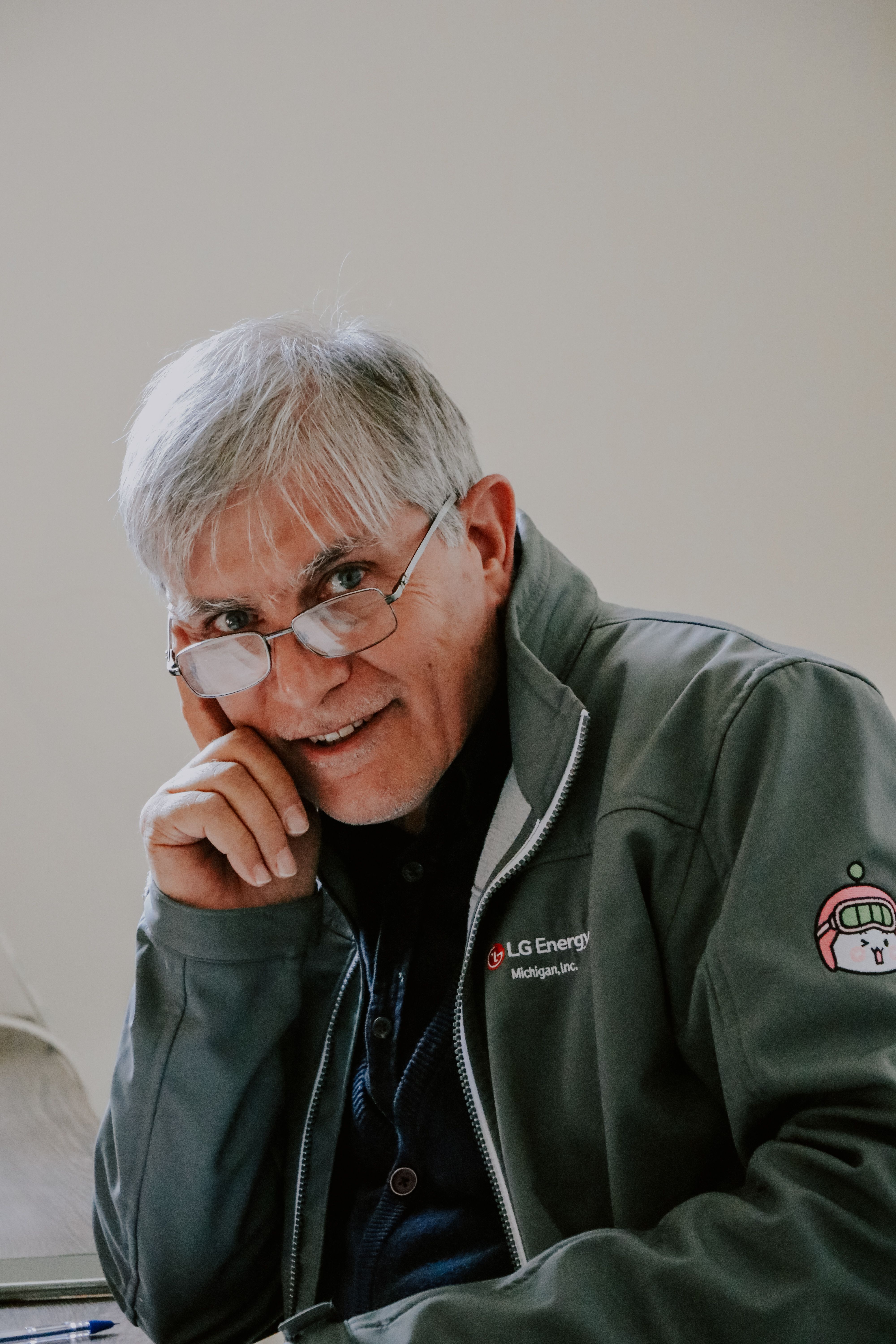 Portrait of a senior man wearing glasses and a jacket with a thoughtful smile, indoors.