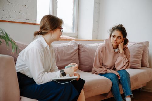 Free A teenager in a hoodie having a therapy session with a female therapist on a sofa. Stock Photo
