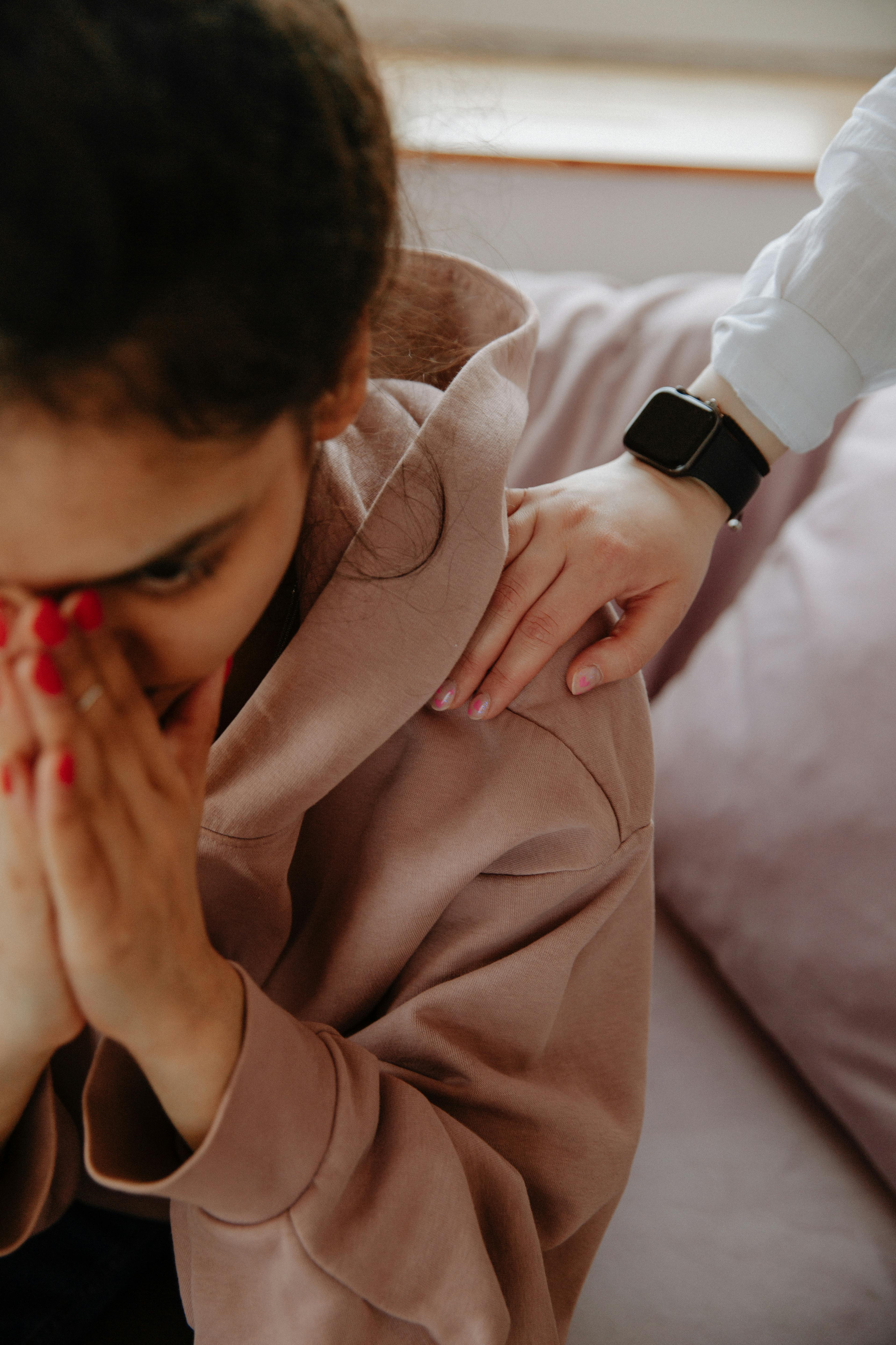 A comforting gesture of support as a hand rests on a young woman's shoulder showing empathy.