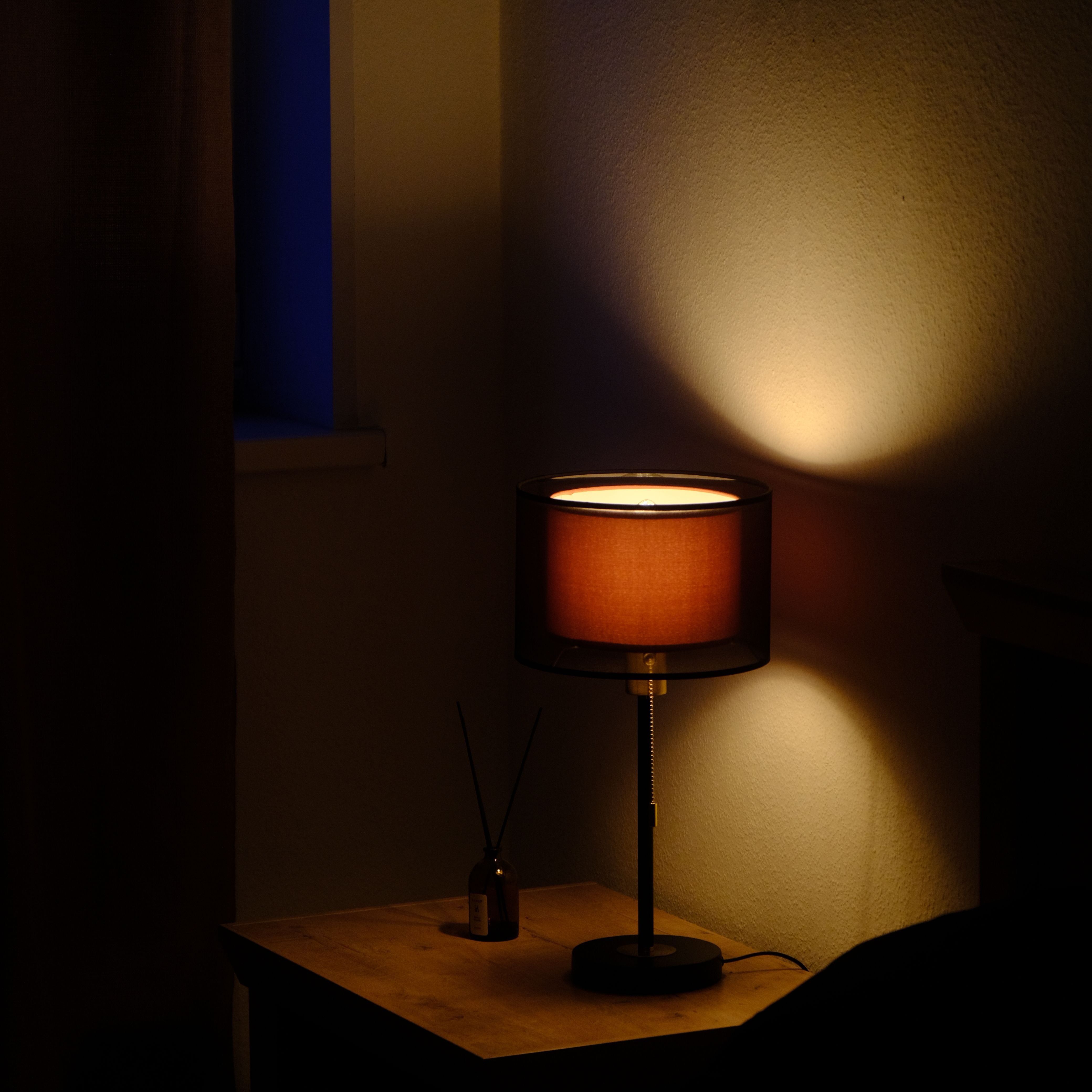 A cozy bedroom scene with a lamp casting warm light on a wall, creating a relaxing ambiance.