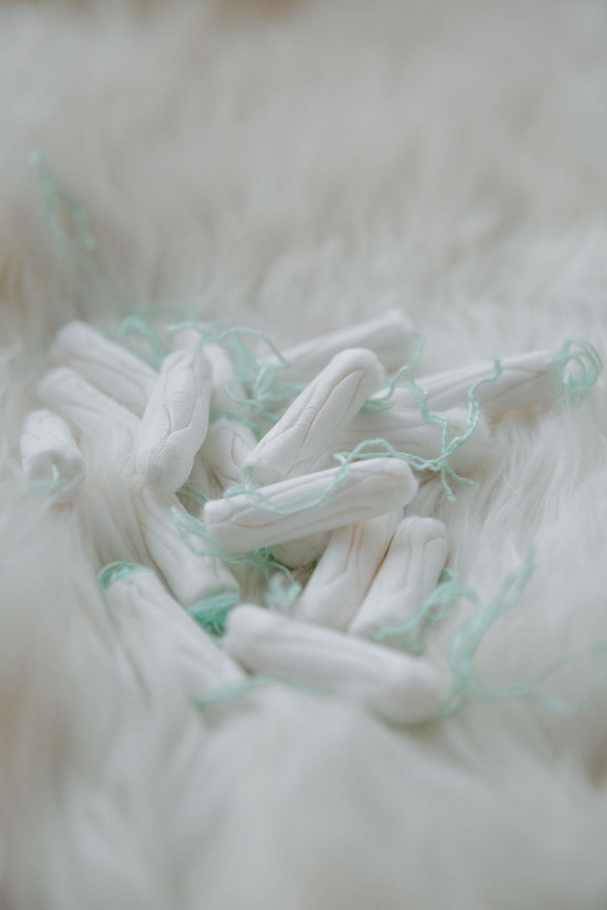 A handful of cotton tampons with pale green strings resting on soft white fabric