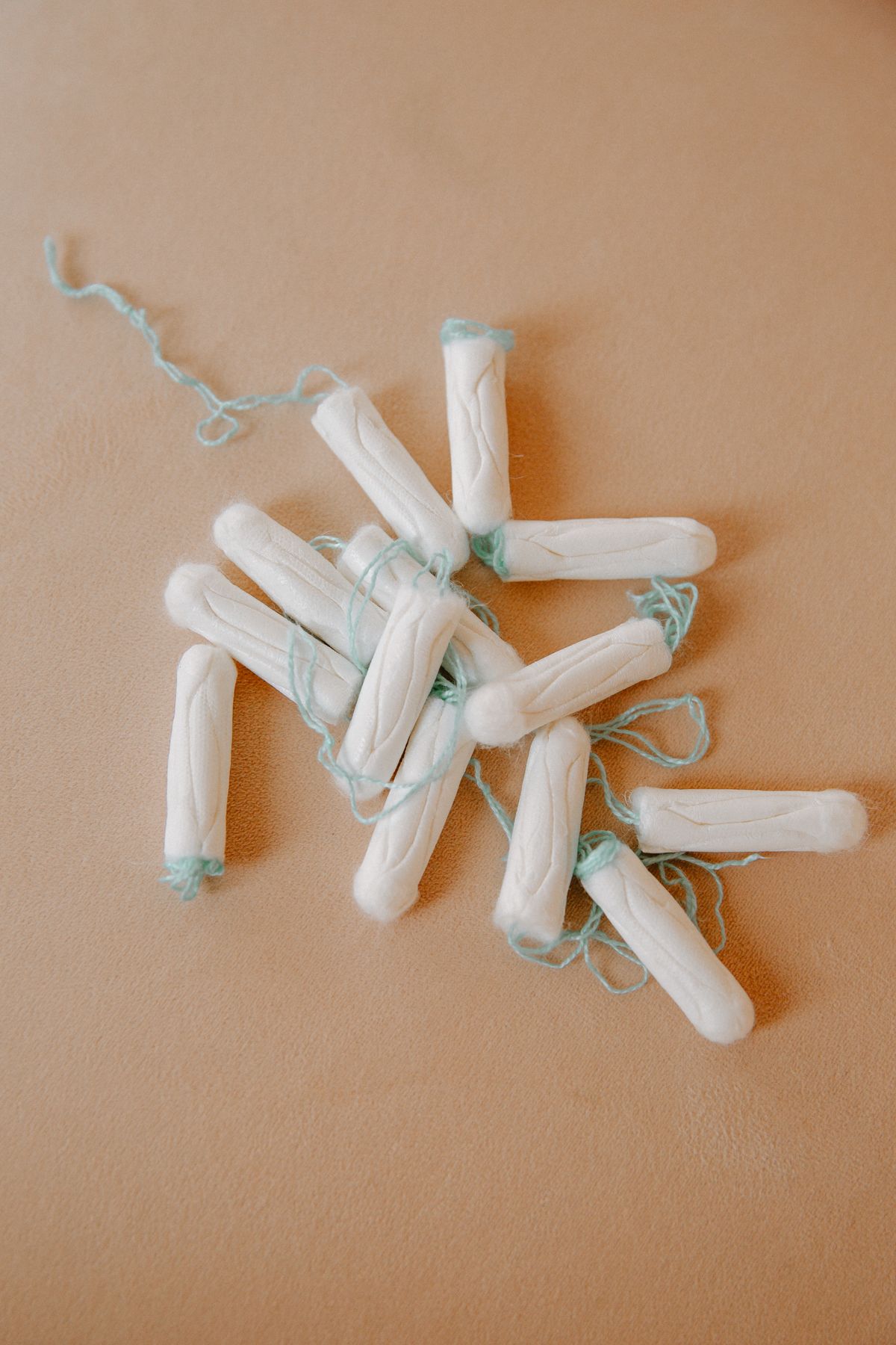 A loose pile of white cotton tampons with pale green strings on a warm beige surface