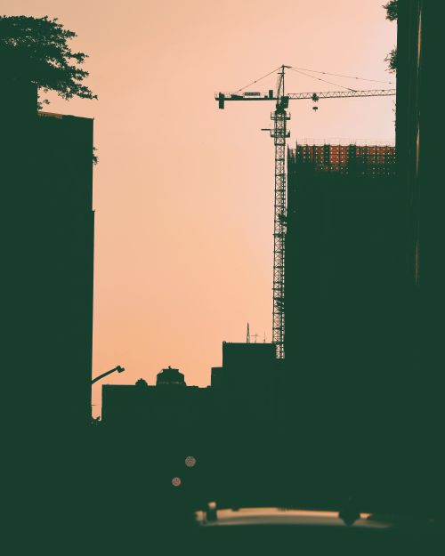 Free Silhouette of a construction crane against a warm sunset sky, highlighting urban development in Taiwan. Stock Photo