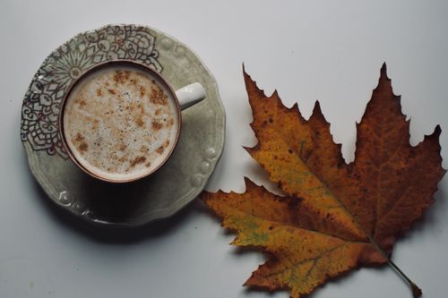 Free A spiced coffee next to a vibrant autumn maple leaf on a white surface. Stock Photo