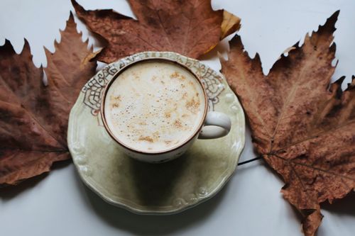 Free Cup of coffee on a plate surrounded by fall leaves on a table. Stock Photo