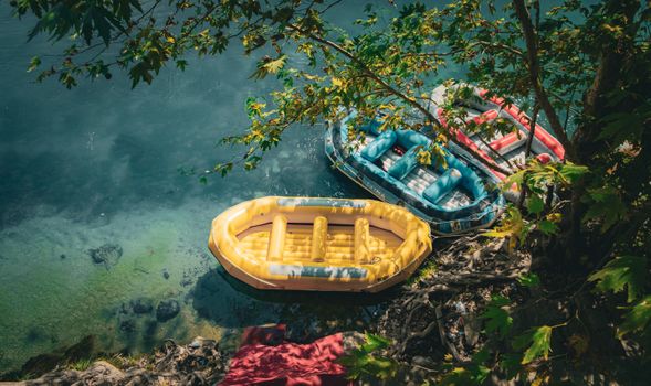 Top-down view of vibrant inflatable rafts on a peaceful, clear river beneath leafy trees.