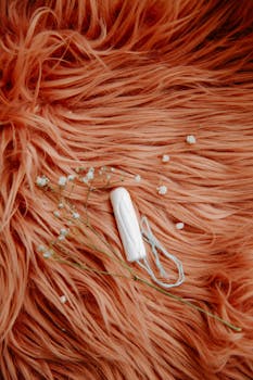 A white tampon with delicate flowers on a soft, textured orange fabric, promoting feminine hygiene.