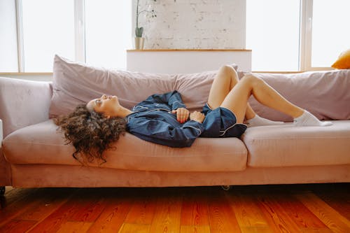 Free Woman Suffering from a Stomach Pain Lying Down on Couch Stock Photo