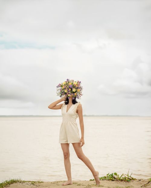 Free Artistic image of a person with a bouquet of flowers for a head, standing by the sea. Stock Photo