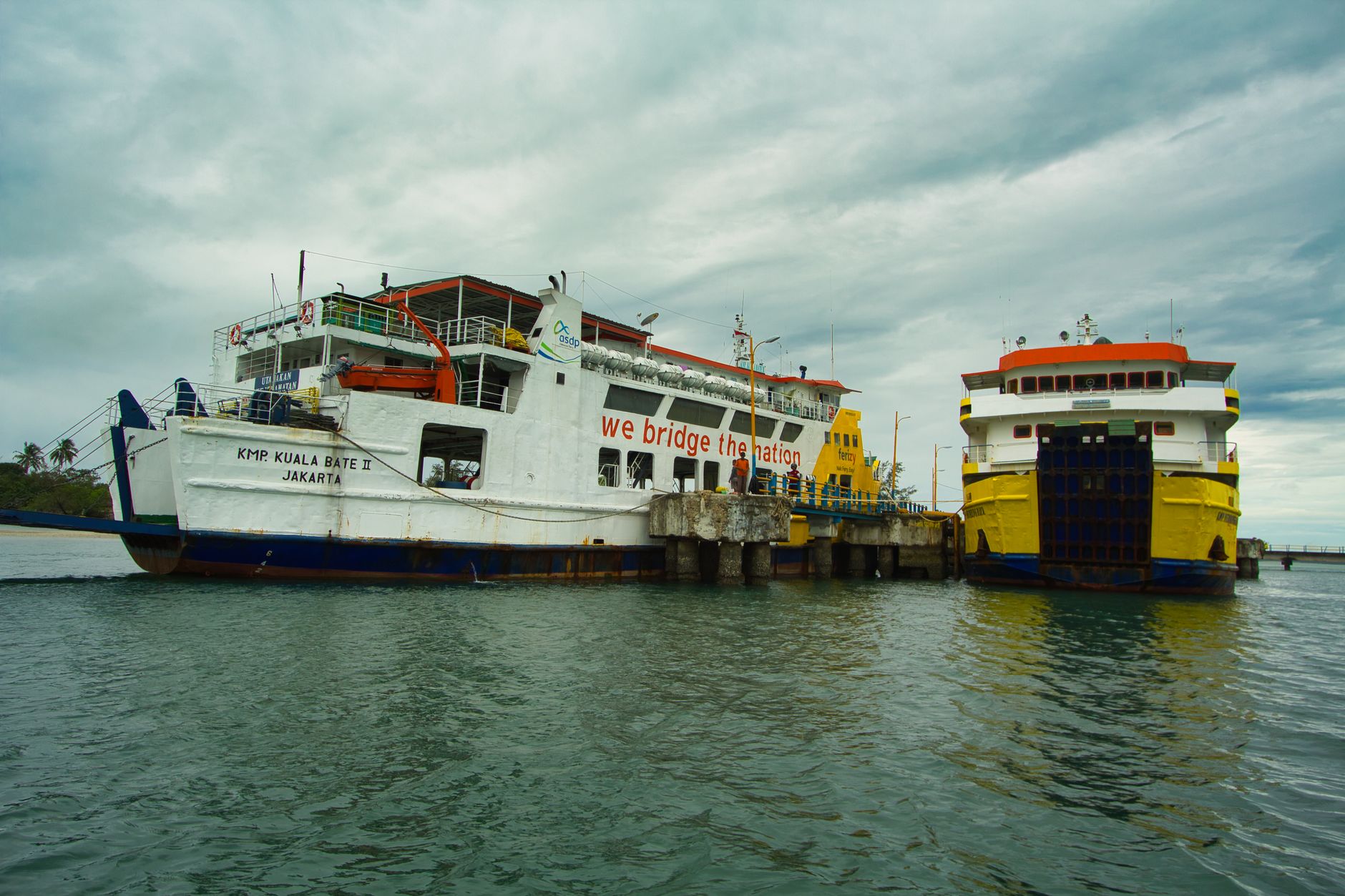 Two ferries docked at Bangka Belitung Islands harbor in Indonesia under cloudy skies.