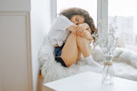 一名年轻女子穿着舒适的服装，蜷缩着坐在窗前，环境舒适宁静