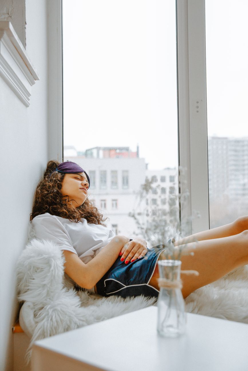 Teenage girl experiencing discomfort while resting by a window at home.
