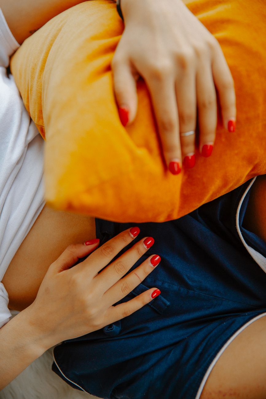 Close-up of a woman's hands comforting herself with a pillow, indicating abdominal pain.