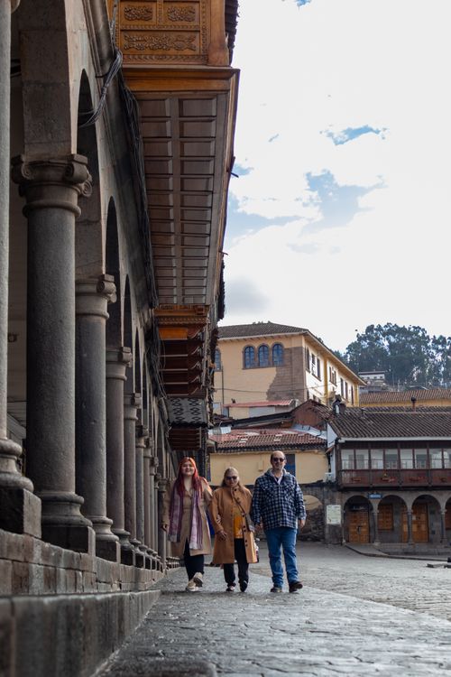 Free Three tourists walk along a historical building with arched columns, capturing a moment of travel exploration. Stock Photo