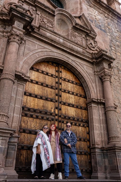 Free Three adults stand in front of a large, ornate wooden door in a classic stone building. Stock Photo