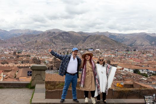 Three adults pose with a panoramic view of Cusco, Peru, showcasing 'Viva El Peru.'
