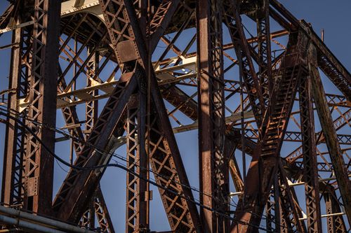 Free Close-up of an aged rusty bridge with intricate steel framework against a clear blue sky. Stock Photo