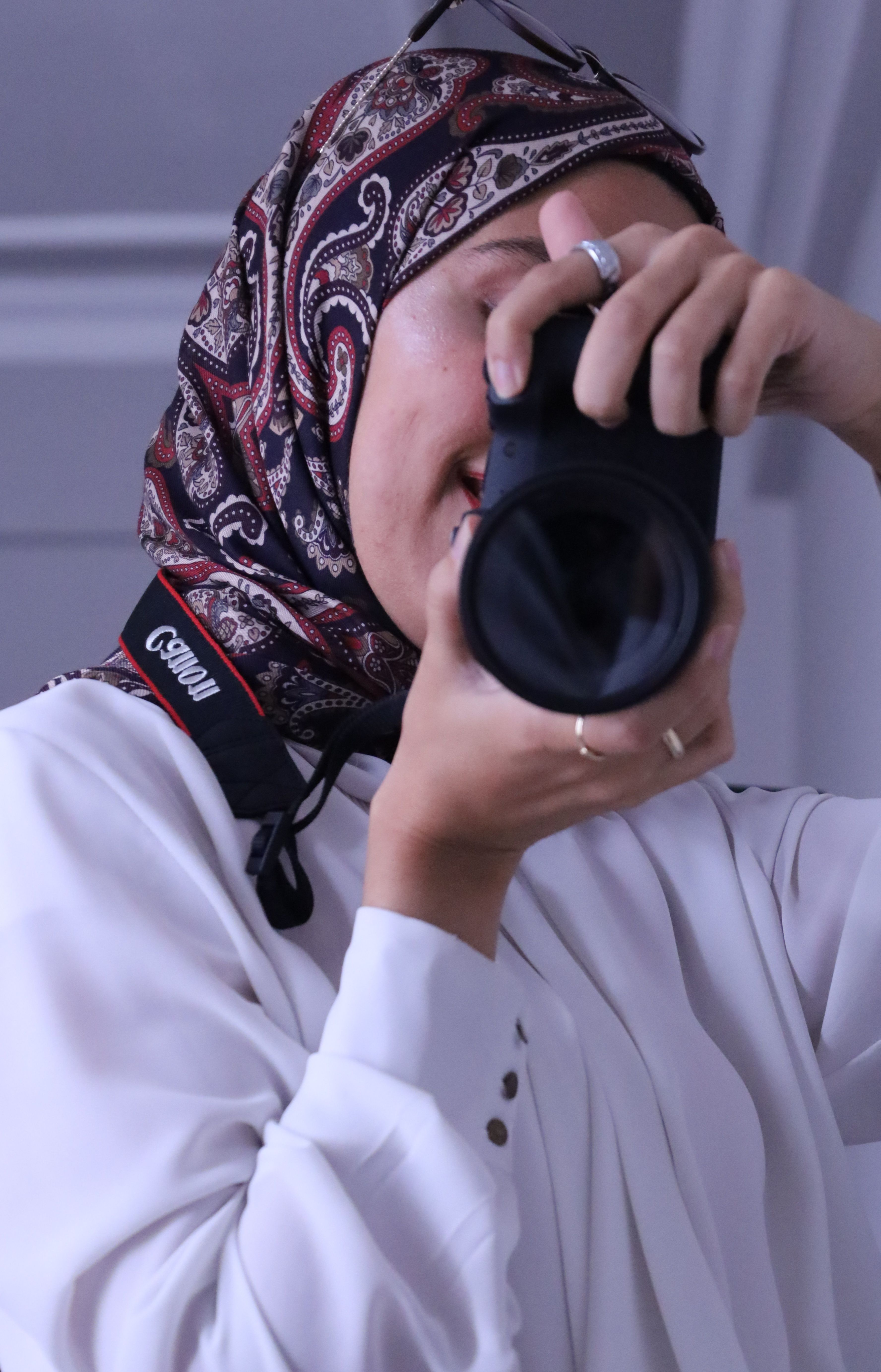 Woman in hijab taking a photo indoors with camera.