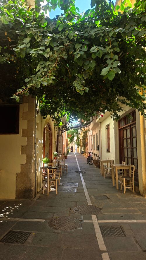 Free Idyllic narrow street in Greece with tables and lush greenery, perfect for a serene walk. Stock Photo