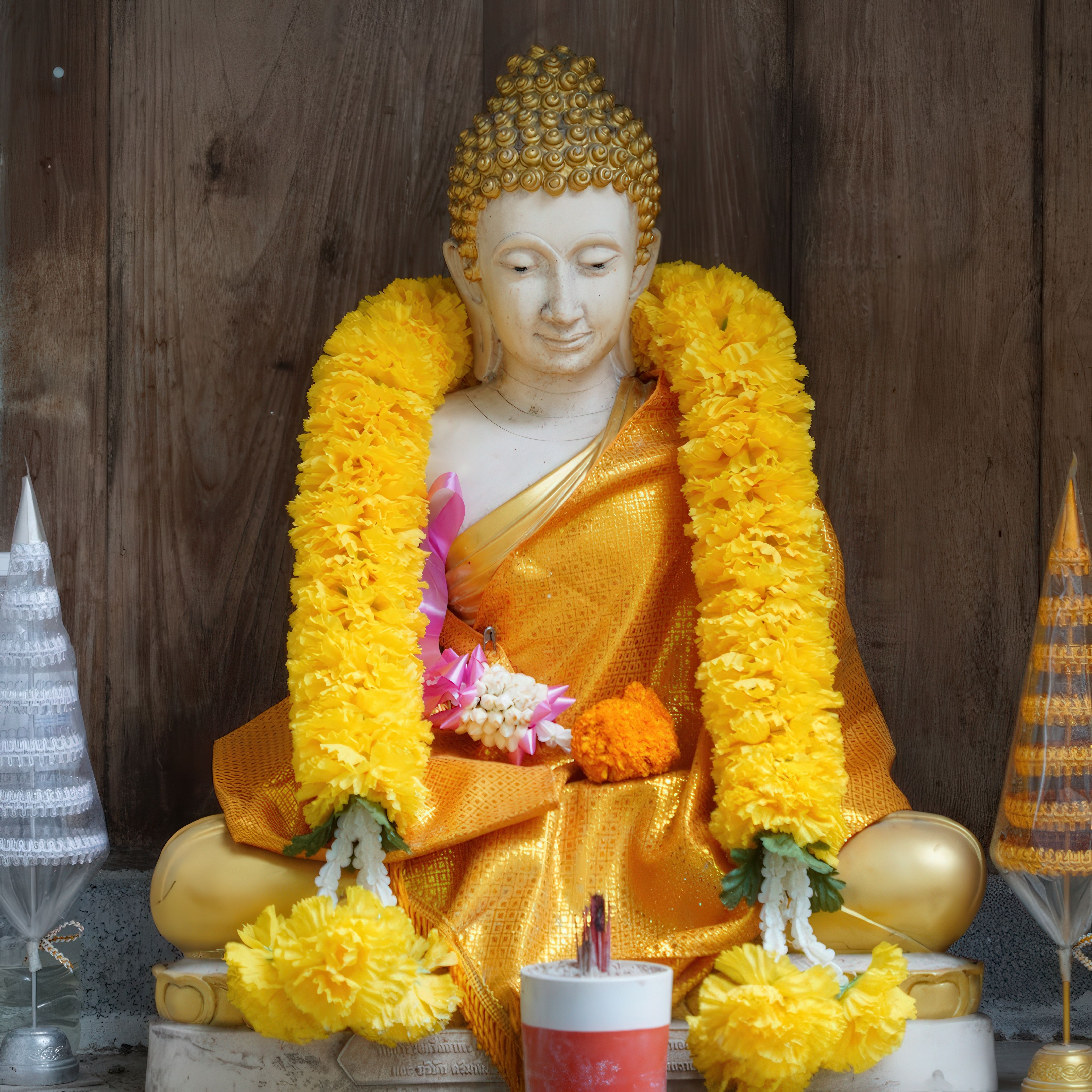 A serene Buddha statue adorned with bright yellow garlands against a wooden backdrop.