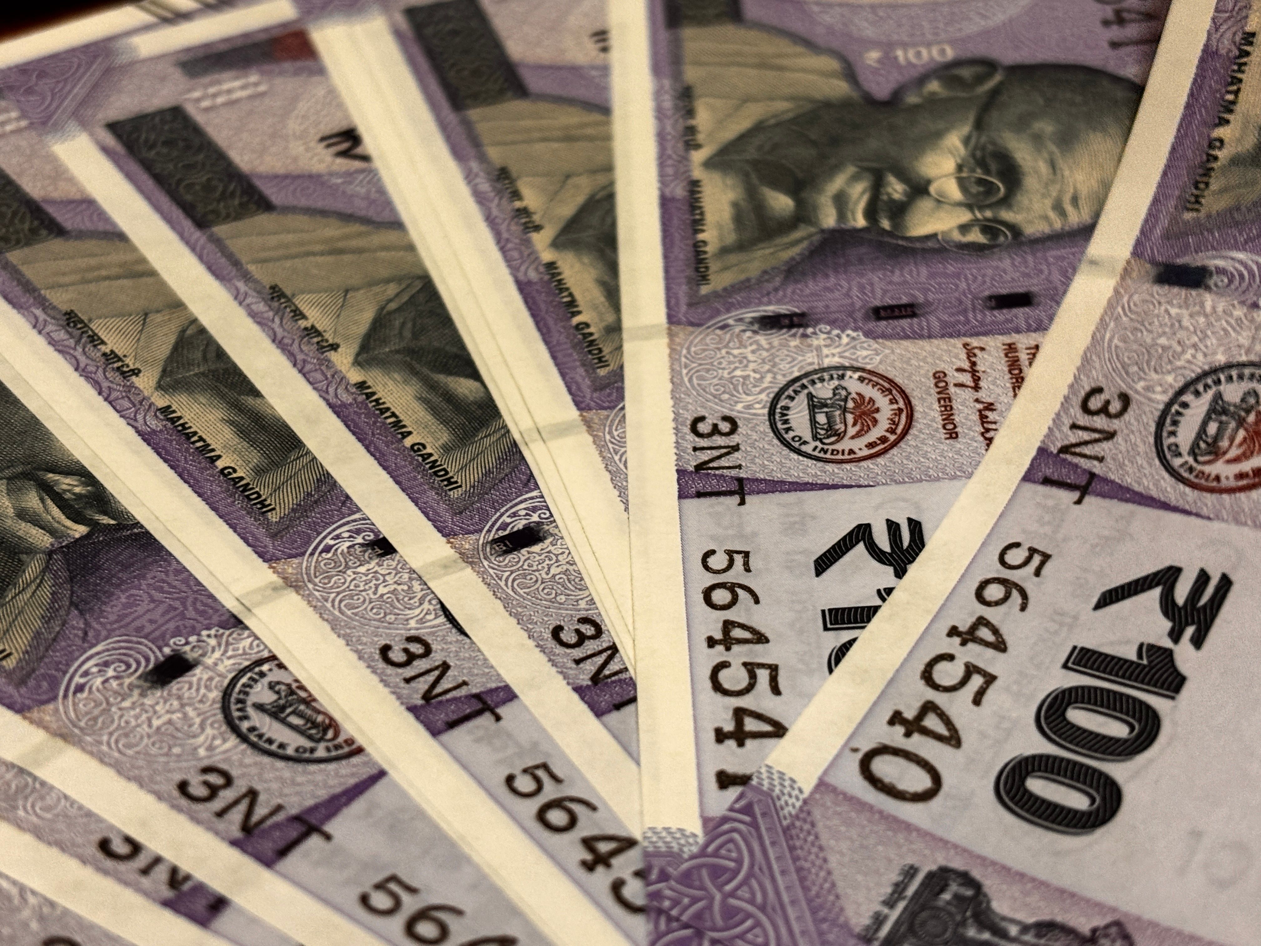 A fan of Indian one-hundred-rupee notes spread across a dark surface, photographed close up.