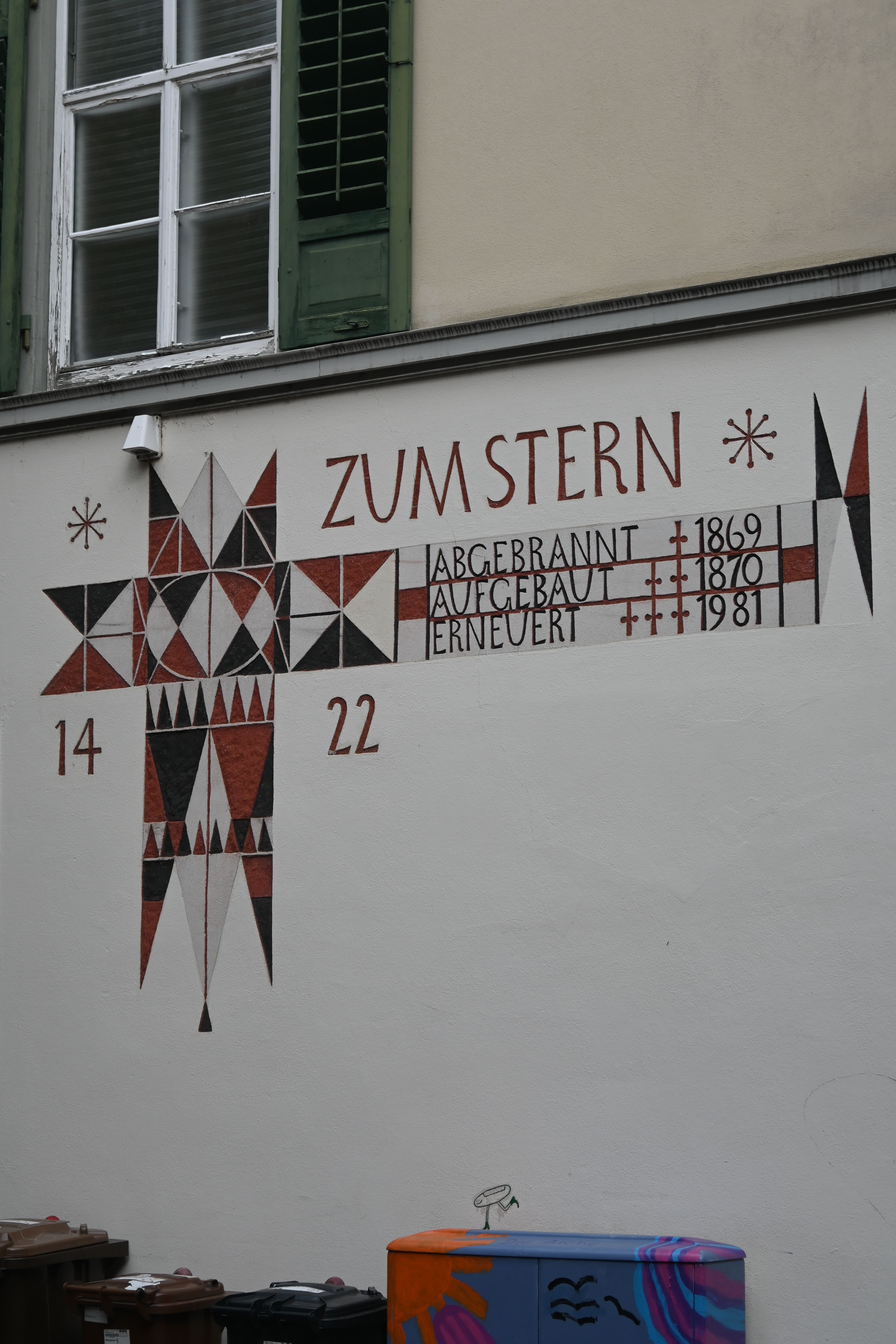 Decorative historical mural on urban building wall with geometric patterns and dates.