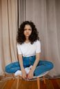 一位年轻女子盘腿坐在室内，肖像展现出一种深思熟虑而富有表现力的情感