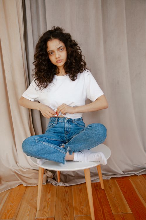 Free A young woman in casual attire poses seated on a chair indoors. Stock Photo