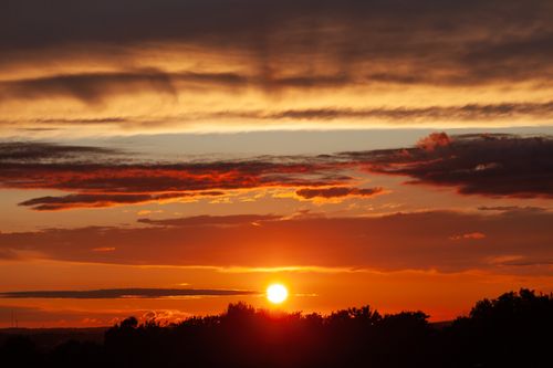 Free A stunning sunset with vivid orange and red hues over a silhouetted forest, creating a dramatic twilight scene. Stock Photo