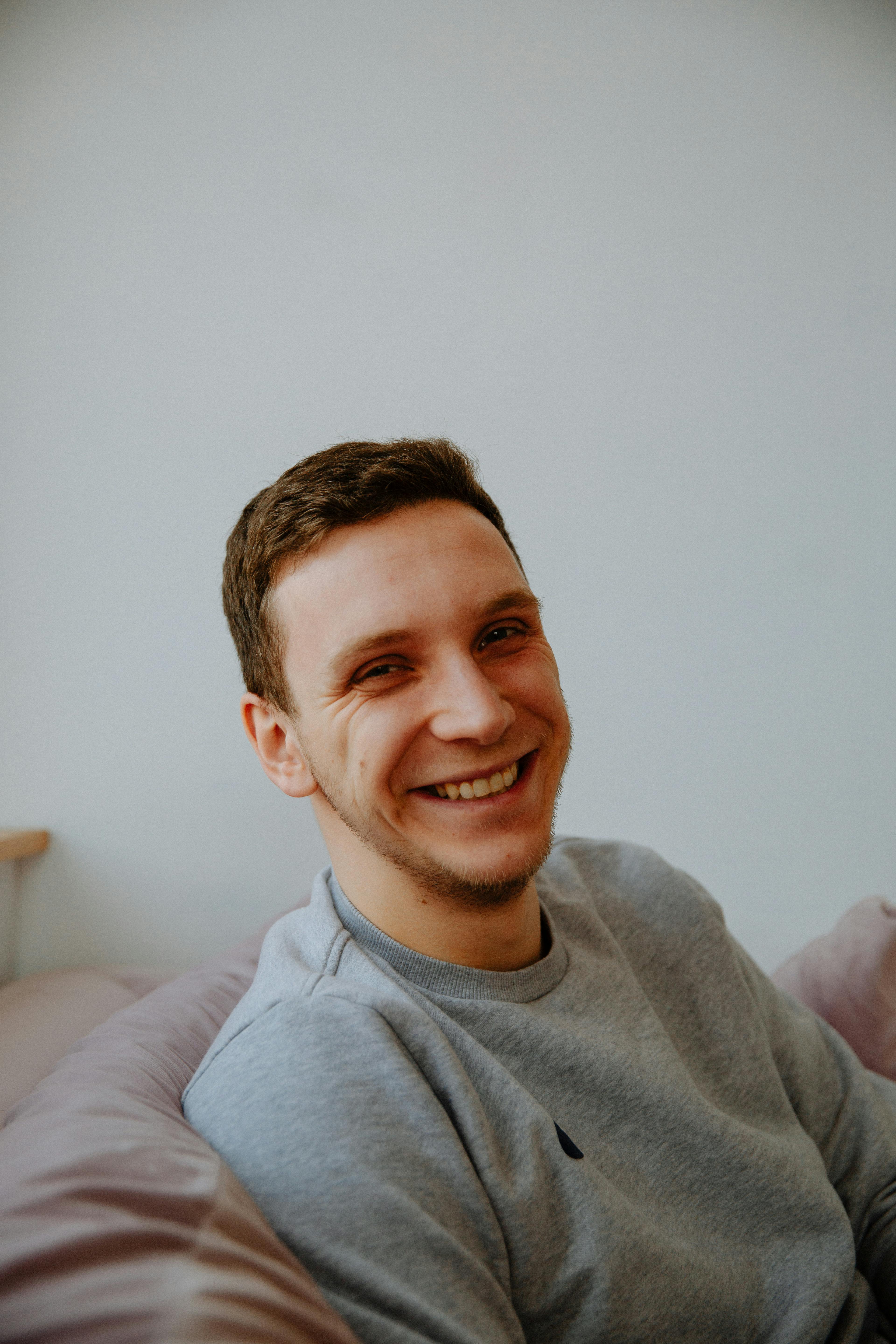 A cheerful man sitting comfortably indoors on a cushioned couch, expressing happiness and relaxation.