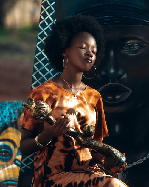 Free Woman in tie-dye dress holding a wooden sculpture in front of African art. Stock Photo