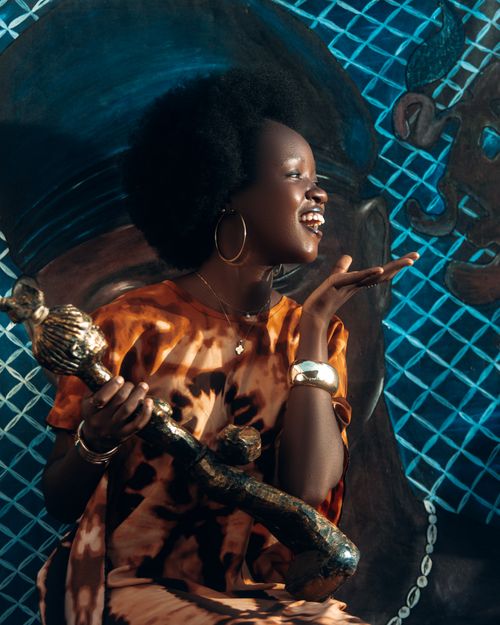 Free A smiling woman in vibrant clothing holds a unique decorative object against a colorful mural background. Stock Photo