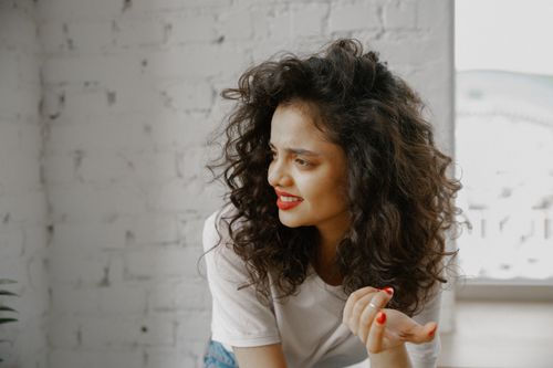 Free Portrait of a young woman with curly hair showing confusion indoors against a white brick wall. Stock Photo