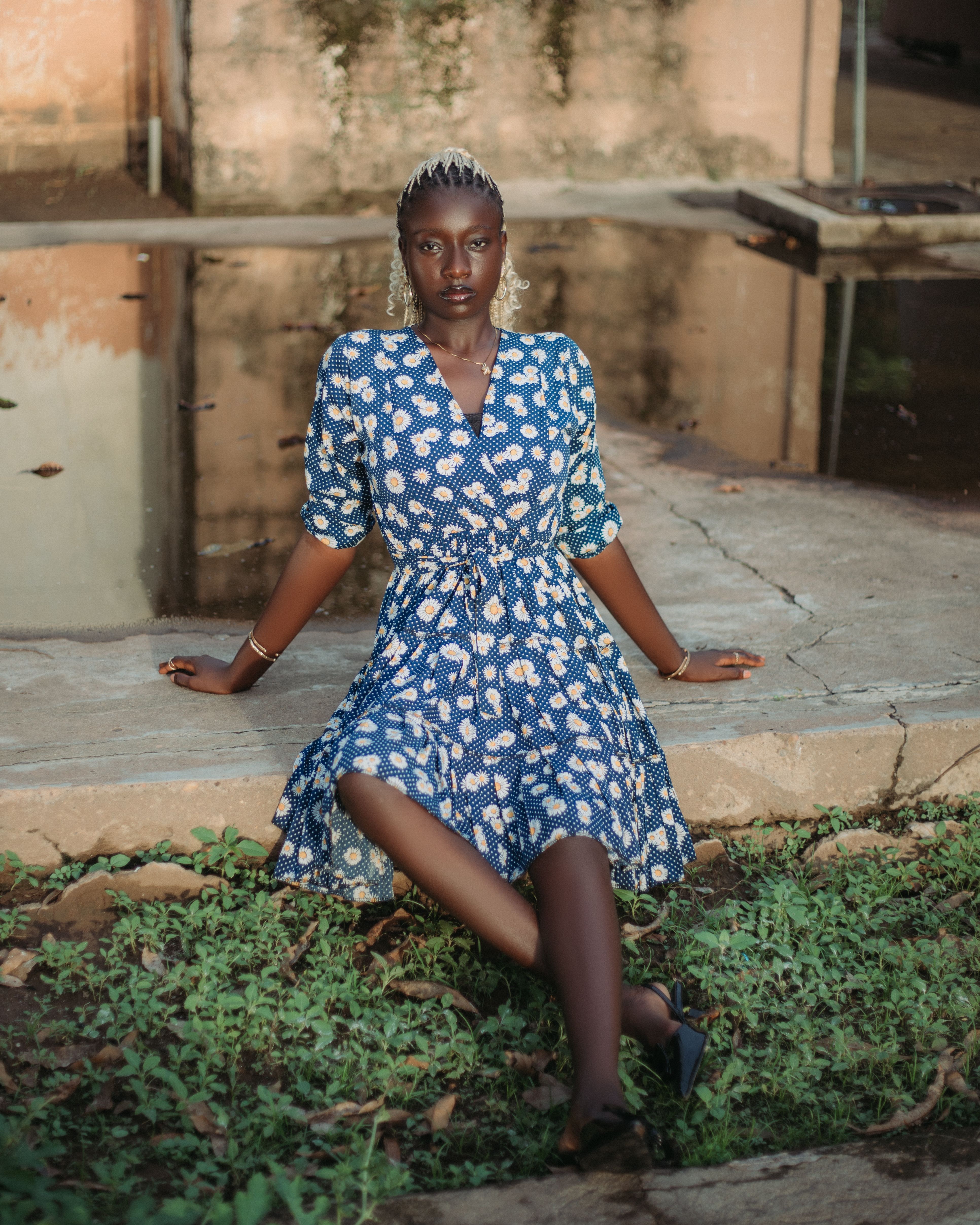 Elegant woman in a blue patterned dress seated by a pond outdoors.