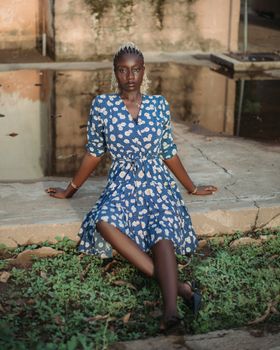 Elegant woman in a blue patterned dress seated by a pond outdoors.