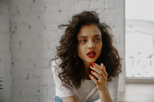 Free A curly-haired woman with red lipstick looks surprised indoors, creating an intense expression. Stock Photo