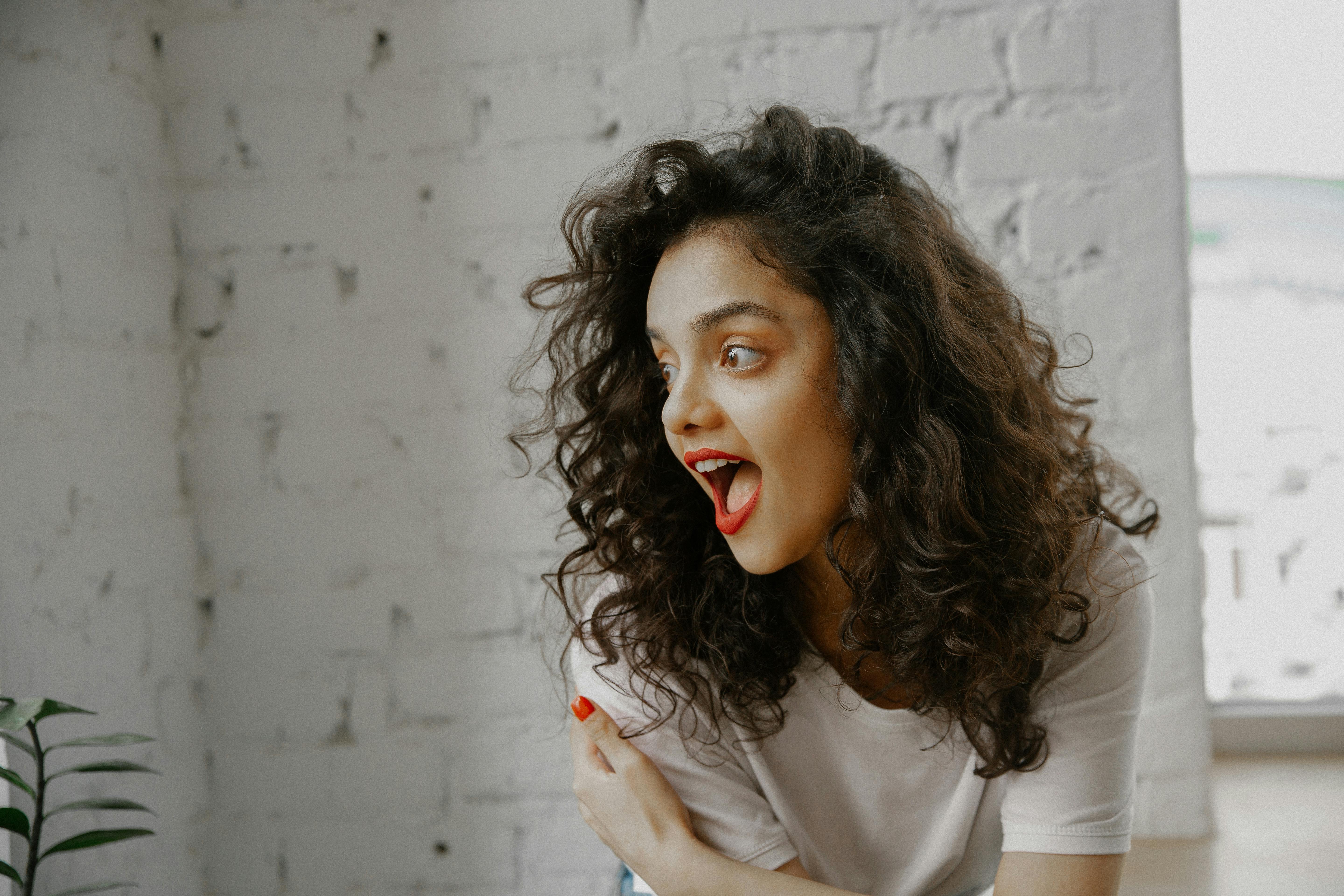 Free Portrait of an excited woman expressing surprise in a bright indoor space. Stock Photo