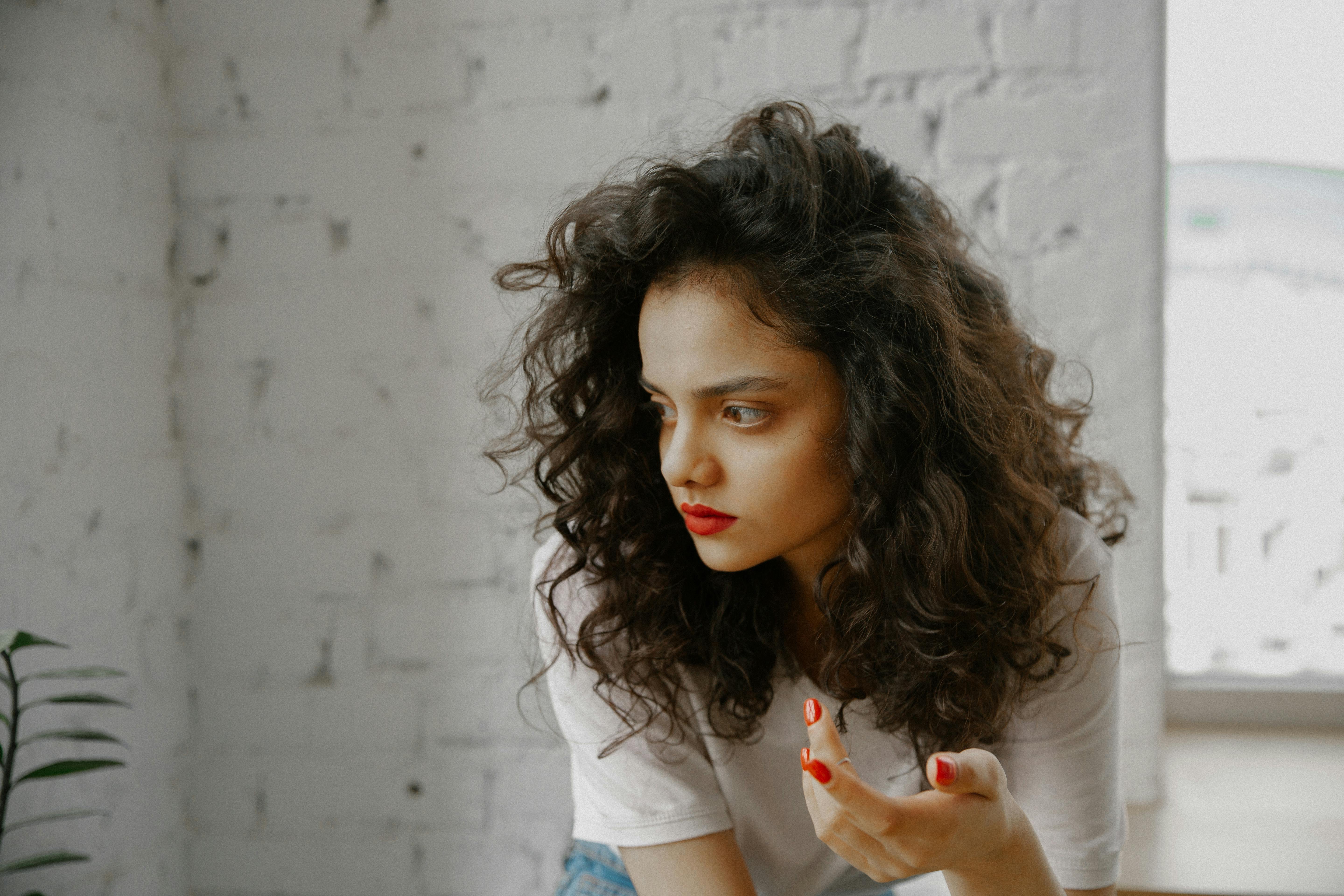 Free Side profile of a fashionable woman with curly hair and red lips deep in thought indoors. Stock Photo