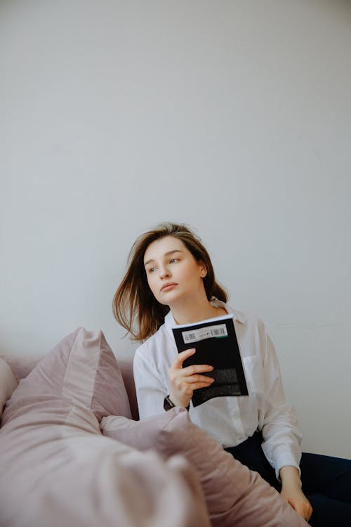 Woman in White Dress Shirt Holding a Black Book