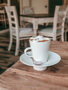 A warm cappuccino with frothy foam sits on a wooden café table, evoking a cozy atmosphere.