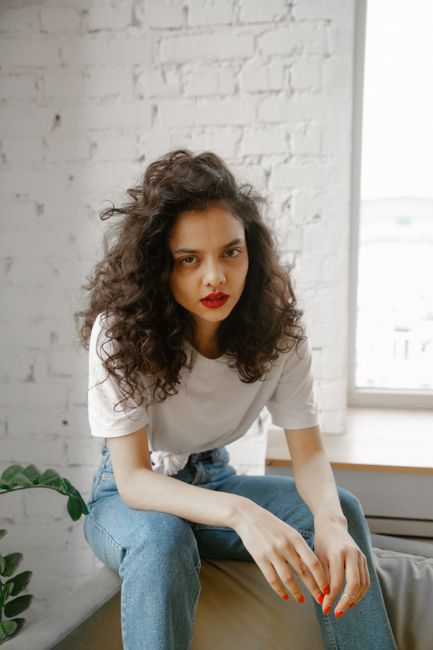 Stylish woman with curly hair sitting indoors, exuding casual elegance and a relaxed vibe.