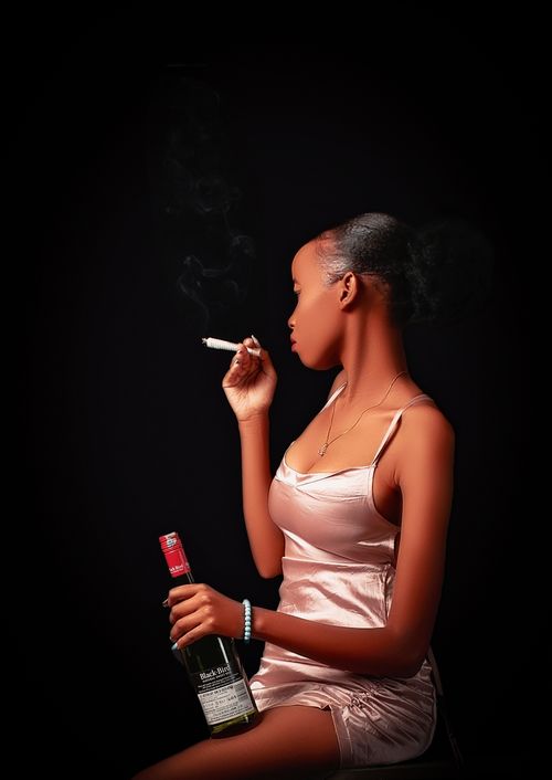Free Stylish woman in satin dress holding a wine bottle and smoking, against a dark background. Stock Photo