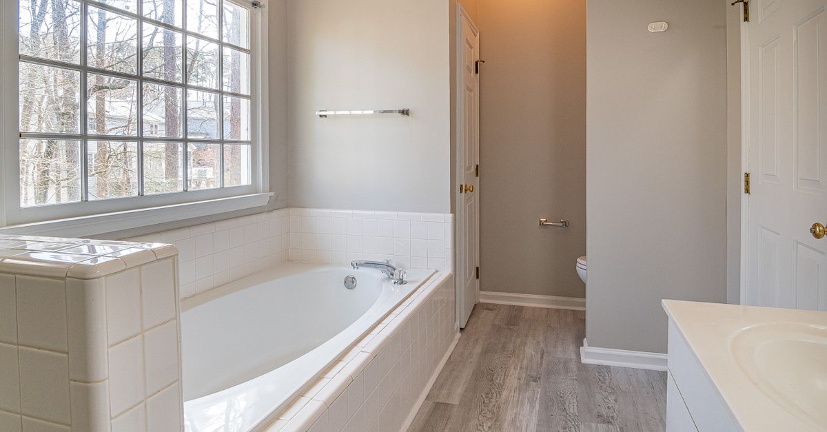 Spacious bathroom featuring a bathtub and bright lighting through a large window.