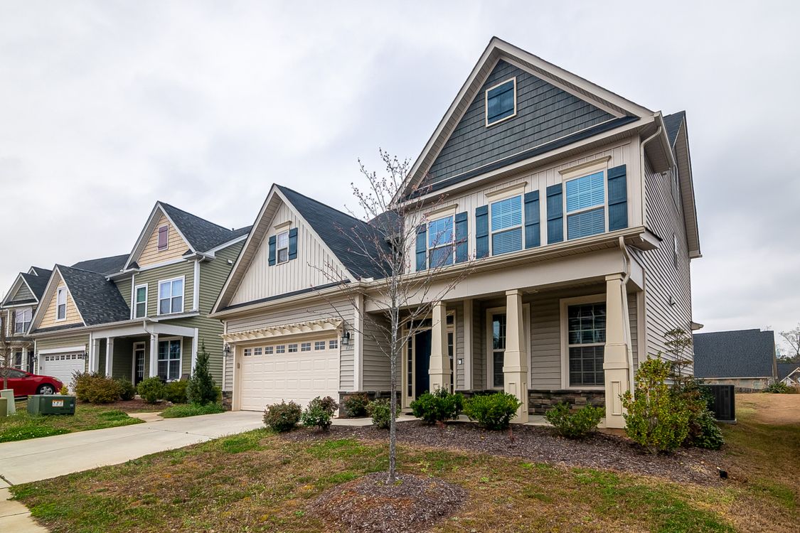 Free A row of modern suburban homes with garages, driveways, and landscaped lawns in daylight. Stock Photo