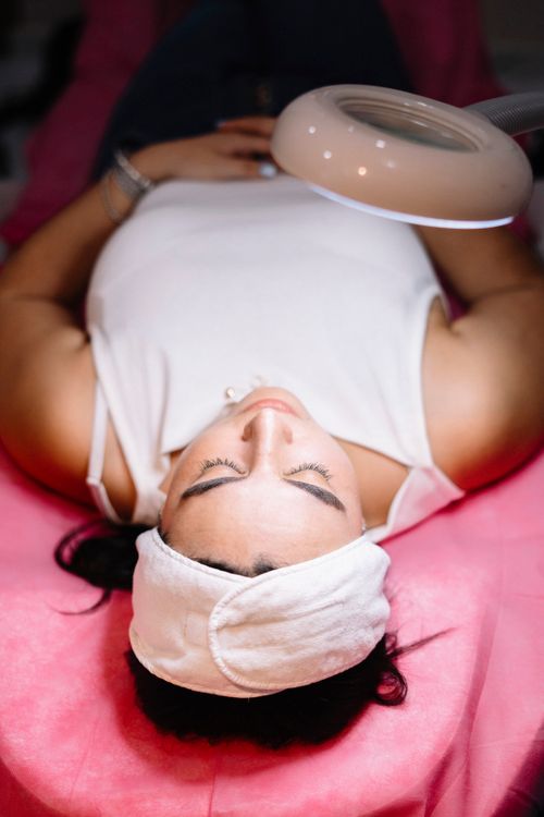 Free A woman enjoys a relaxing facial treatment in a spa, under a magnifying lamp, providing a calm ambiance. Stock Photo