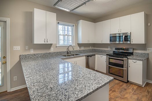 Sleek kitchen design featuring granite countertops, white cabinets, and stainless steel appliances.