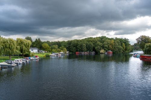 Free Tranquil lakeside with boats docked under a dramatic sky, perfect for nature lovers. Stock Photo