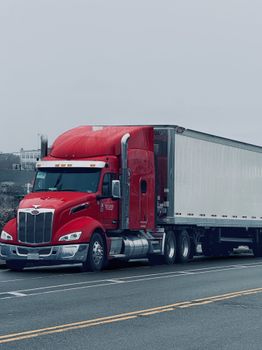 Vibrant red semi-truck on a deserted highway under cloudy skies. Ideal for logistics themes.